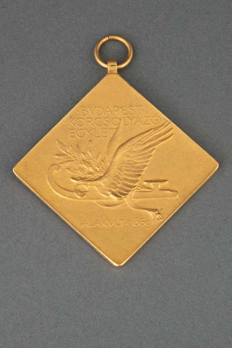 Kvadratisk medalje i gull med opphøyet rand og punslet dekor. På avers er det fremstilt to løpende skøyteløpere og på revers en bevinget skøyte og en laurbærgren.