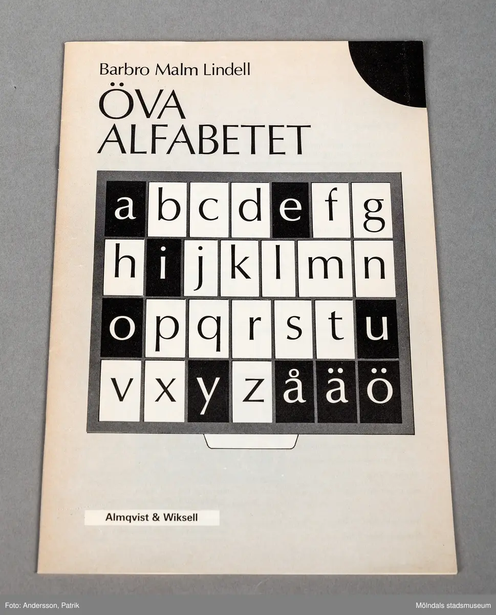 Ett mindre tunnt häfte. På framsidan finns en svart vit bild på en nästan kvadratisk ruta som innehåller olika stora rutor som innehåller alfabetet i ordning frå A-Ö.
Framsidan har en svart markering i högra övre hörnet.