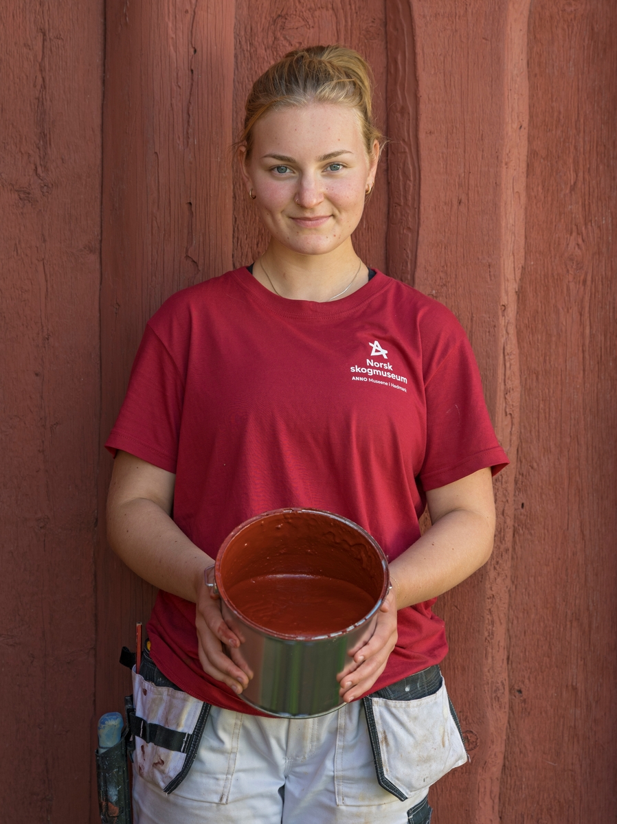 Portrett av Marie Randen, hospitant hos Glomdalsmuseet via Norsk håndverksinstitutt, i forbindelse med at hun kokte maling under De nordiske jakt- og fiskedagene 2023 på Norsk skogmuseum i  Elverum, Hedmark, Innlandet. Malingen som ble produsert fra bunnen av var rød komposisjonsmaling, og malingen ble brukt til å male en vegg på en av museets bygninger.