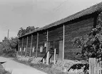 En större ladugård med nedplockat taktegel som ligger på marken mot väggen.