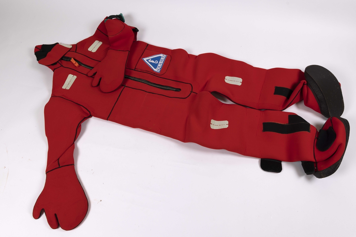 Overlevelesdrakt produsert i neopren trolig 1980-1990 årene. Redningsdrakt med integrert hette, hansker og støvler. Glidelås i front med påmontert fløyte. Ligger i en orange oppbevaringsbag.