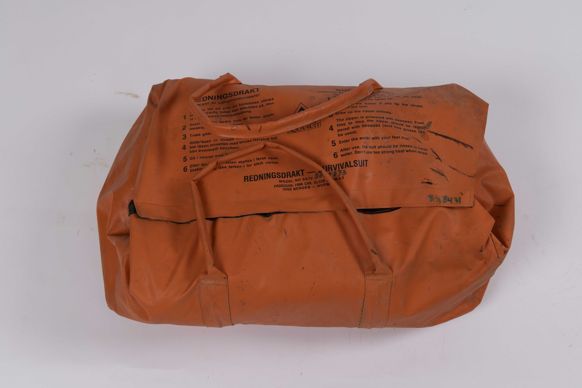 Overlevelesdrakt produsert i neopren trolig 1980-1990 årene. Redningsdrakt med integrert hette, hansker og støvler. Glidelås i front med påmontert fløyte. Ligger i en orange oppbevaringsbag.