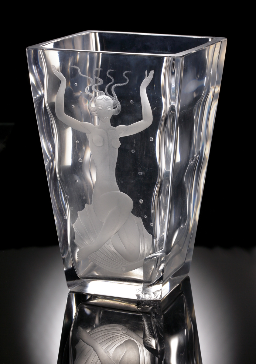Formgivare Vicke Lindstrand. Tjockväggig bägare/vas med kvadratisk konande form. Främre vägg graverat med ett
undervattensmotiv föreställande Venus.
