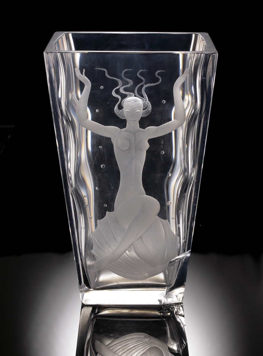 Formgivare Vicke Lindstrand. Tjockväggig bägare/vas med kvadratisk konande form. Främre vägg graverat med ett
undervattensmotiv föreställande Venus.