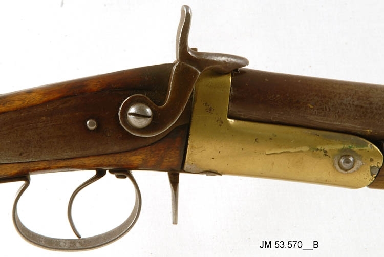 Hagelbössa, en så kallad stiftantändare, även kallad "Hovslättsbössan", tillverkad omkring år 1900. Avsett för stiftantändning. Piplängd 796 mm. Kaliber 16 mm, hyllslängd 6 cm. Tillverkningsnummer (vapennummer) saknas, men om pipan fälls ner syns numret 26 stämplat i metallen. Försedd med vapenrem av läder. Orört originalvapen. 

På kolven är inskuret mönster vid handgreppet och årtalet "1912" Detta är gjort av den tidigare ägaren Jesper Gustavsson. Årtalet avser det år vapnet kom till familjen Gustavsson.

Tillhörande Deklarationsbevis nr 139, år 1934 för målaren Verner Gustav Oskar Gustavsson, Åsa Lilla, Sandseryds socken.

Tillbehör:
1. Patronutdragare (ringformad)
2. Patronutdragare (nyckelformad)
3. Patroner, 15 st
4. Rengöringsdon i snöre
5. Ask med lösa hagel
6. Krok (dubbelkrok/hatthylla)