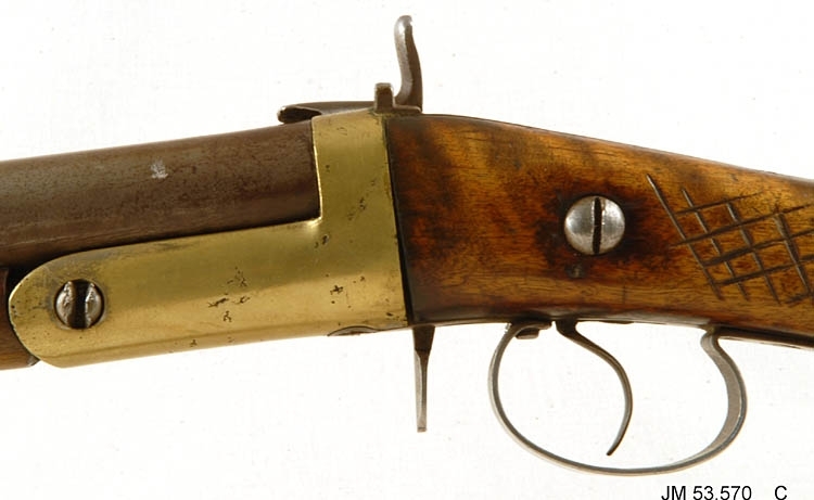 Hagelbössa, en så kallad stiftantändare, även kallad "Hovslättsbössan", tillverkad omkring år 1900. Avsett för stiftantändning. Piplängd 796 mm. Kaliber 16 mm, hyllslängd 6 cm. Tillverkningsnummer (vapennummer) saknas, men om pipan fälls ner syns numret 26 stämplat i metallen. Försedd med vapenrem av läder. Orört originalvapen. 

På kolven är inskuret mönster vid handgreppet och årtalet "1912" Detta är gjort av den tidigare ägaren Jesper Gustavsson. Årtalet avser det år vapnet kom till familjen Gustavsson.

Tillhörande Deklarationsbevis nr 139, år 1934 för målaren Verner Gustav Oskar Gustavsson, Åsa Lilla, Sandseryds socken.

Tillbehör:
1. Patronutdragare (ringformad)
2. Patronutdragare (nyckelformad)
3. Patroner, 15 st
4. Rengöringsdon i snöre
5. Ask med lösa hagel
6. Krok (dubbelkrok/hatthylla)