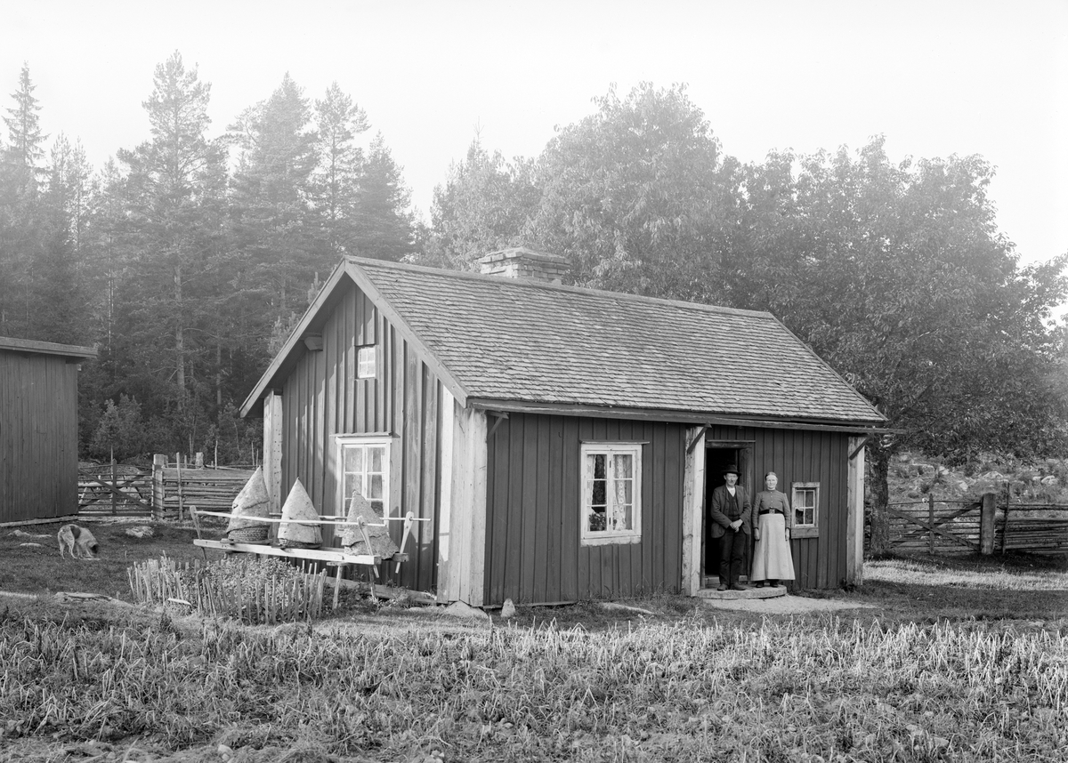 Lilla Kvarntorpet på Attarps ägor i Svinhult. I dörröppningen ses brukarna av det före detta soldattorpet, makarna Sven Peter och Hanna Skog. Sven Peter hade kommit hit redan 1876, då som livgrenadjär. Hanna Maria flyttade in i samband med parets giftemål 1880. Vid indelningsverkets avskaffande 1901, omändrades Kvarntorpet till ett ordinärt torp. Notera bikuporna av halm som placerats intill gavelväggen.