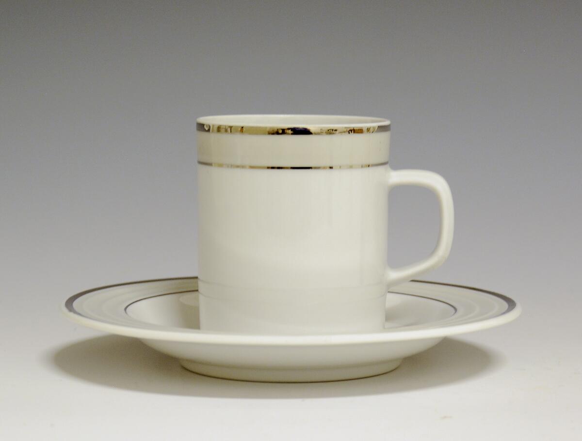 Kopp av porselen med hvit glasur. Dekorert med to enkle striper i platina med et grått bånd i mellom øverst på korpus.
Modell: Saturn
Dekor: Platina
