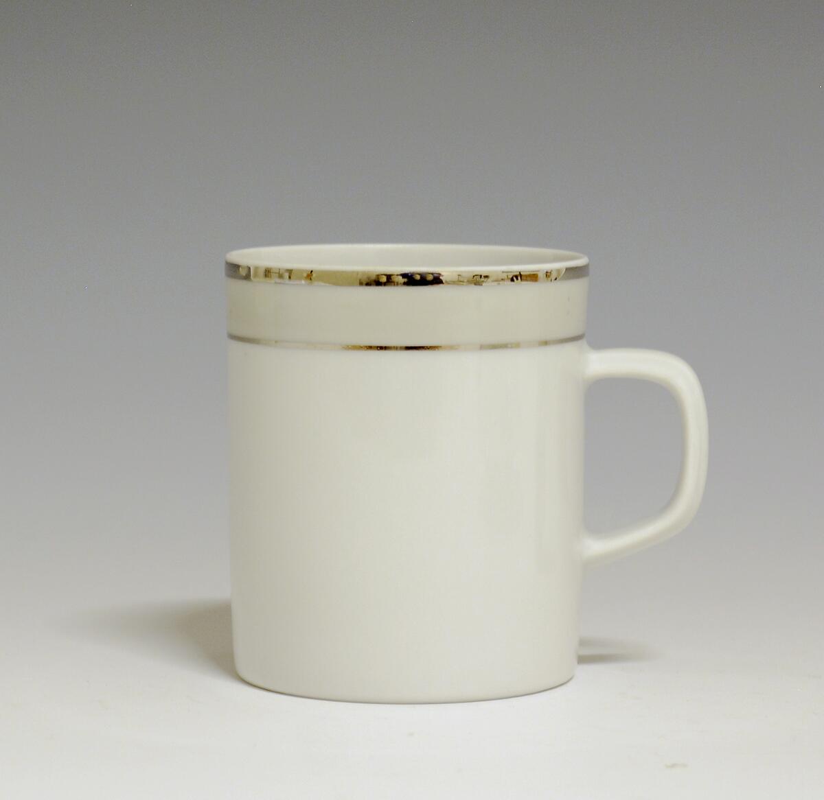 Kopp av porselen med hvit glasur. Dekorert med to enkle striper i platina med et grått bånd i mellom øverst på korpus.
Modell: Saturn
Dekor: Platina
