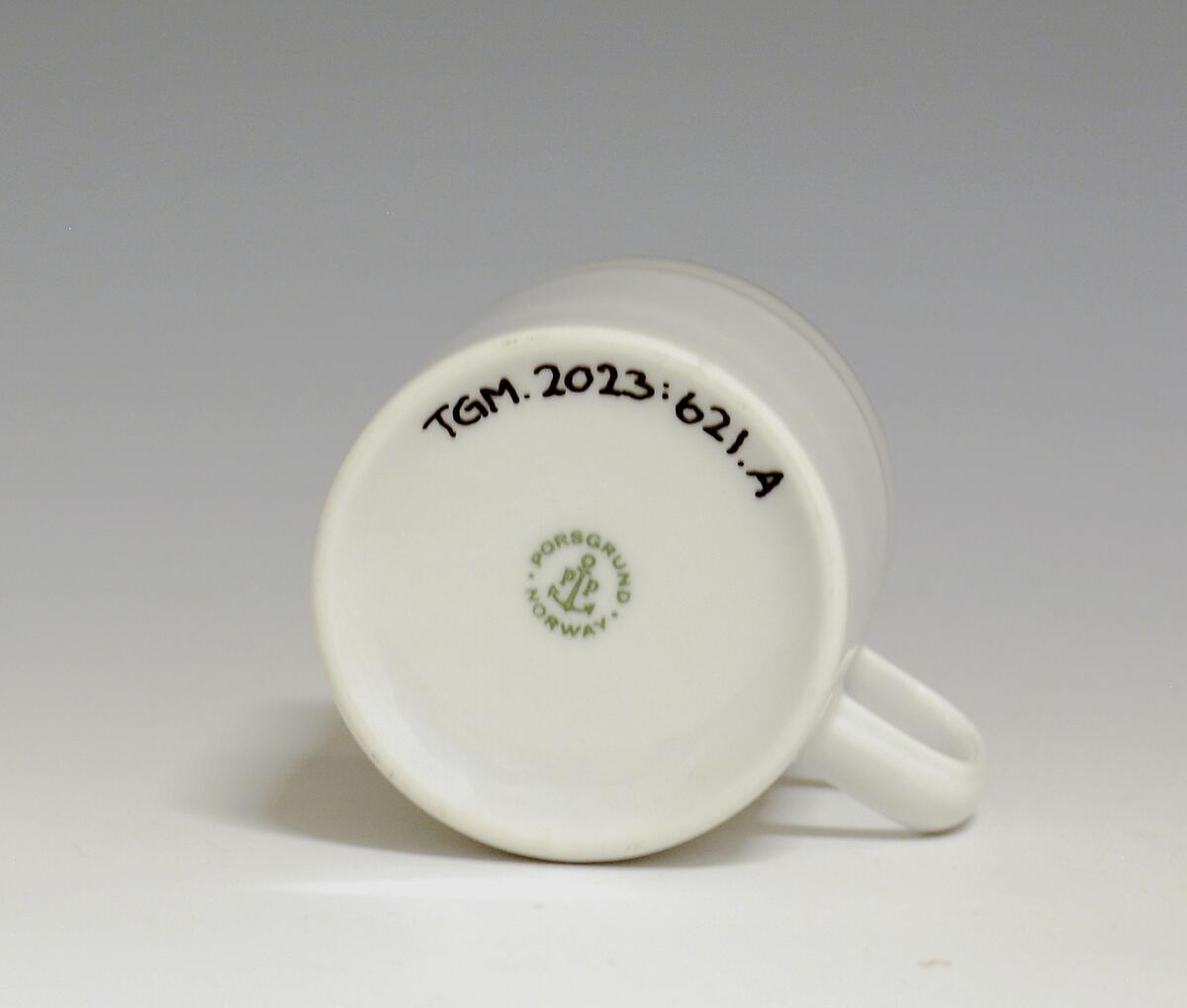 Kopp av porselen med hvit glasur. Dekorert med to enkle striper i platina med et grått bånd i mellom øverst på korpus.
Modell: Saturn
Dekor: Platina
