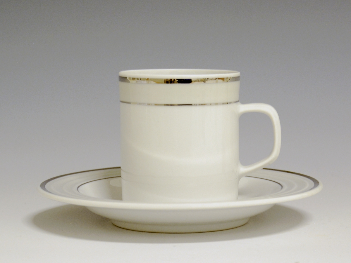 Kopp av porselen med hvit glasur. Dekorert med to enkle striper i platina med et grått bånd i mellom øverst på korpus.
Modell: Saturn
Dekor: Platina
