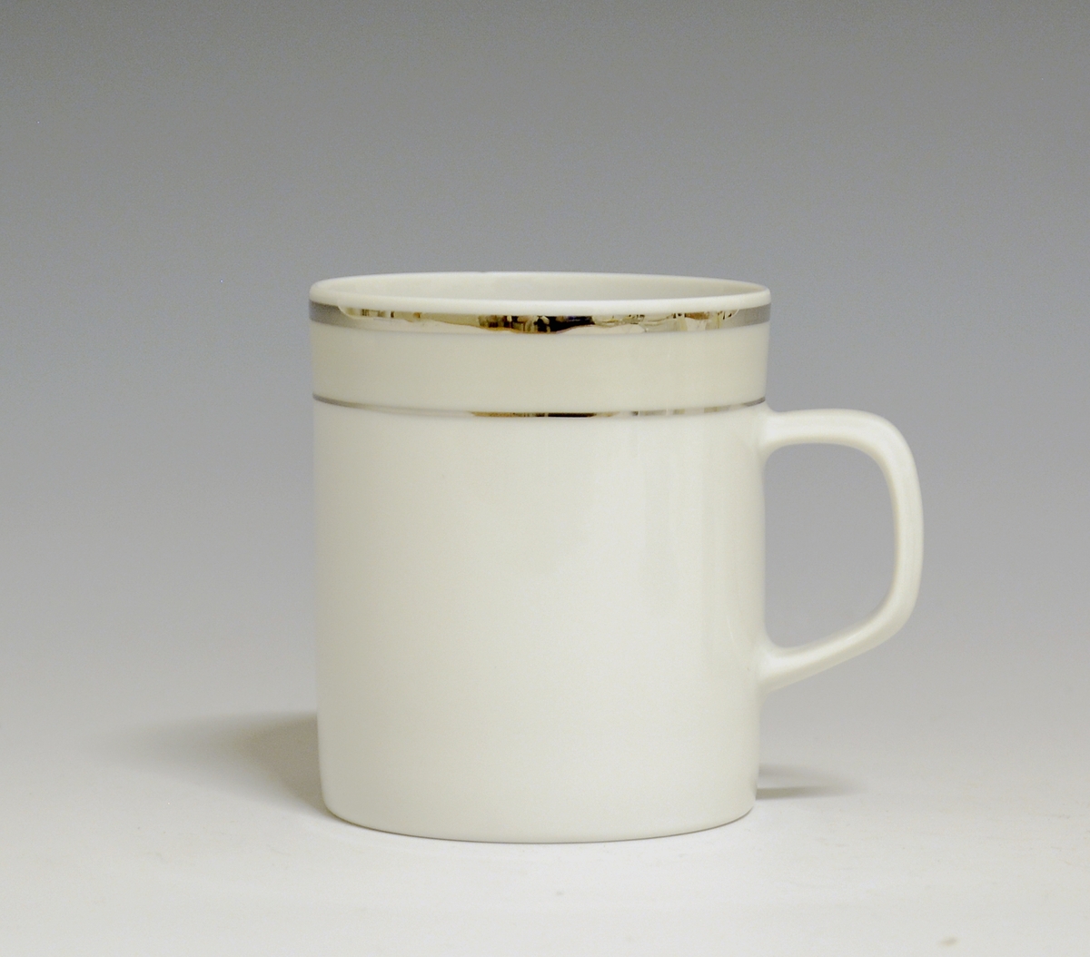 Kopp av porselen med hvit glasur. Dekorert med to enkle striper i platina med et grått bånd i mellom øverst på korpus.
Modell: Saturn
Dekor: Platina
