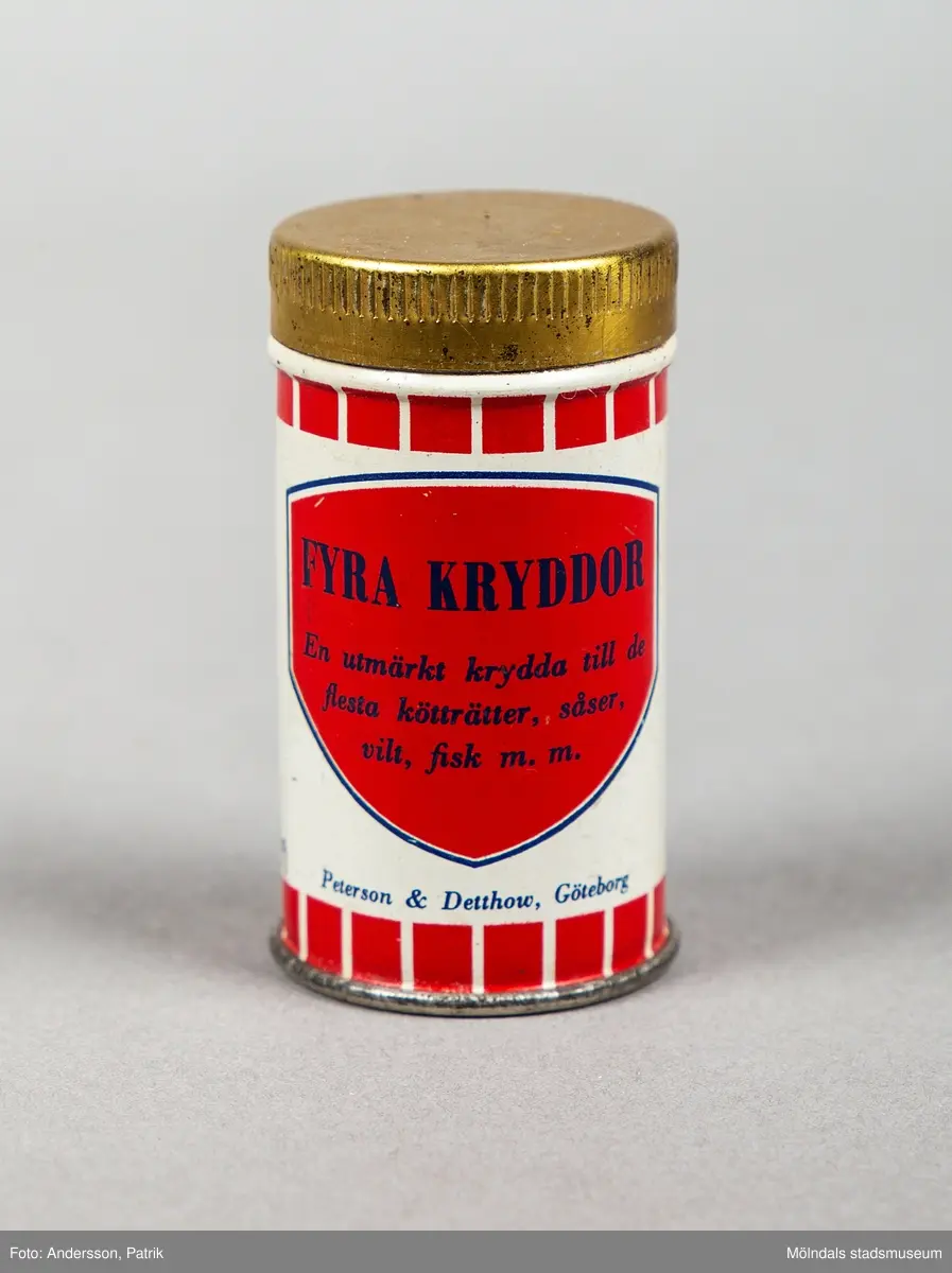 En cylinderformad plåtburk med tryckt dekor i rött och svart. Locket är guldfärgat.  Tryckt rubrik "fyra kryddor". Motsidan har text: INREGISTR.VARUMÄRKE med tomte vid en stor mortel. Därunder finns texten En utmärkt kryddatill de flesta kötträtter, såser, vilt,fisk m.m.