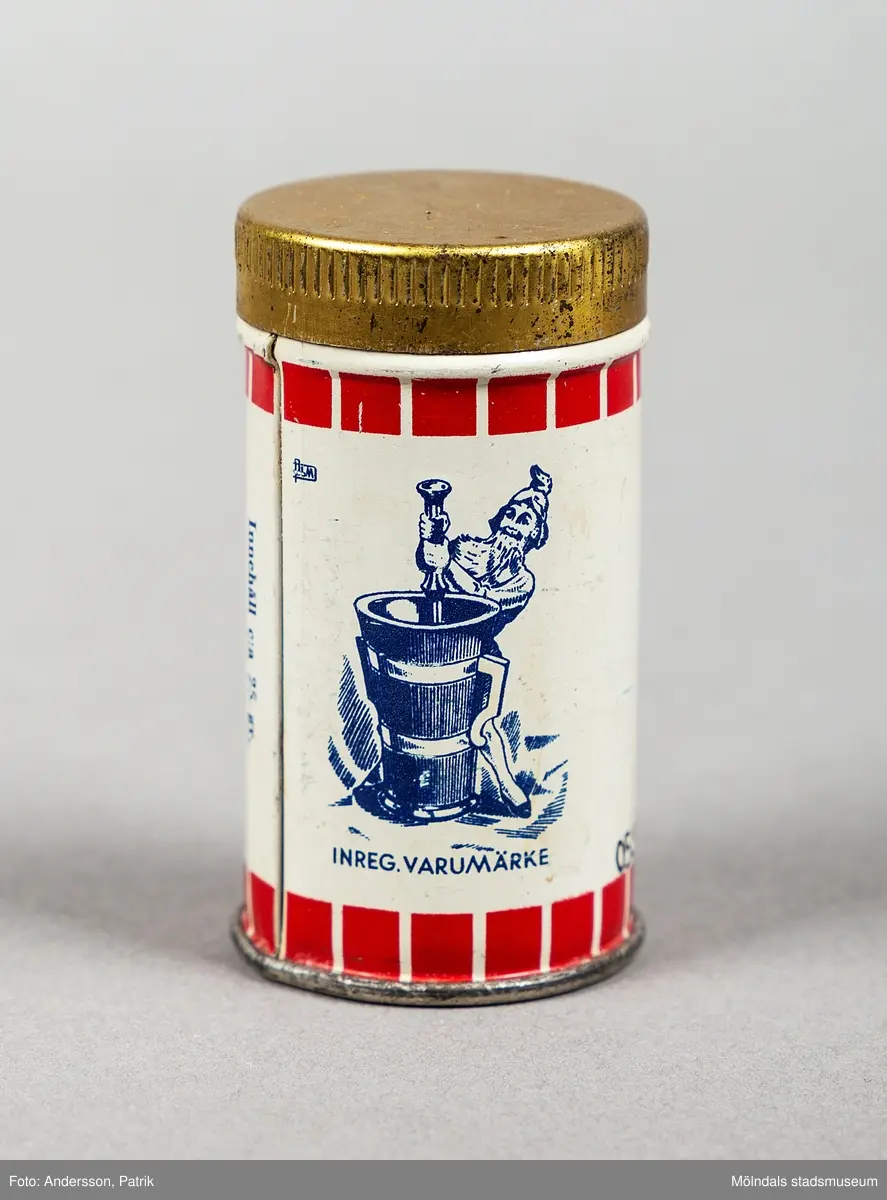 En cylinderformad plåtburk med tryckt dekor i rött och svart. Locket är guldfärgat.  Tryckt rubrik "fyra kryddor". Motsidan har text: INREGISTR.VARUMÄRKE med tomte vid en stor mortel. Därunder finns texten En utmärkt kryddatill de flesta kötträtter, såser, vilt,fisk m.m.