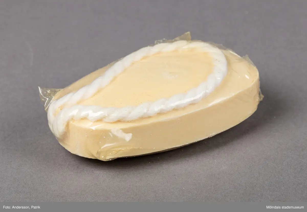 En genomskinlig plastförpackning som innehåller en upphängningsbar badtvål. Badtvålen är vaniljgul och har ett vitt snurrat rep för upphängning fäst i tvålens ände.
På askens framsida finns en guldfärgad oval dekal. På dekalen finns en innehållsdeklaration.
Det finns också en stor inramad ruta med angivet pris. På askens sida finns företagsnamnet Åhlens Tempo angivet.
Tvålen är tillverkad av företaget Victoria som började tillverka tvålar redan 1914.