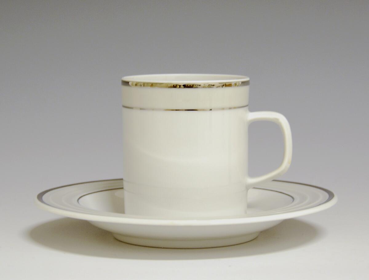 Kopp av porselen med hvit glasur. Dekorert med to enkle striper i platina med et grått bånd i mellom øverst på korpus.
Modell: Saturn
Dekor: Platina
