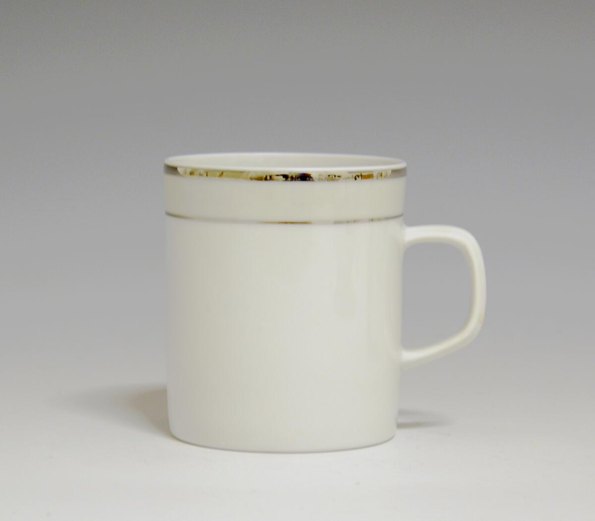 Kopp av porselen med hvit glasur. Dekorert med to enkle striper i platina med et grått bånd i mellom øverst på korpus.
Modell: Saturn
Dekor: Platina
