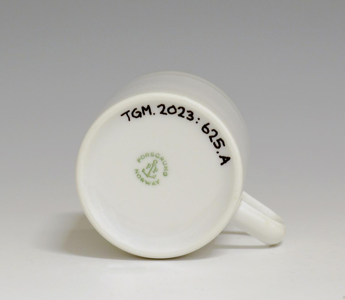 Kopp av porselen med hvit glasur. Dekorert med to enkle striper i platina med et grått bånd i mellom øverst på korpus.
Modell: Saturn
Dekor: Platina
