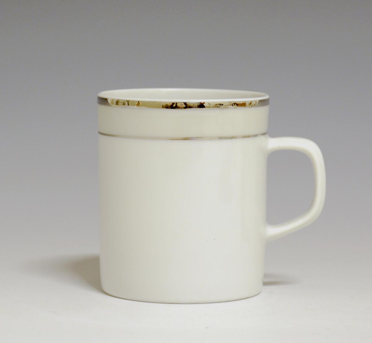 Kopp av porselen med hvit glasur. Dekorert med to enkle striper i platina med et grått bånd i mellom øverst på korpus.
Modell: Saturn
Dekor: Platina
