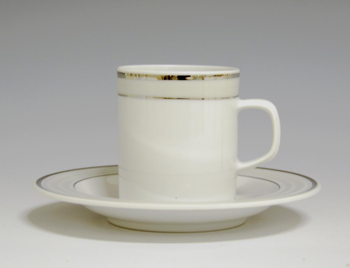 Kopp av porselen med hvit glasur. Dekorert med to enkle striper i platina med et grått bånd i mellom øverst på korpus.
Modell: Saturn
Dekor: Platina
