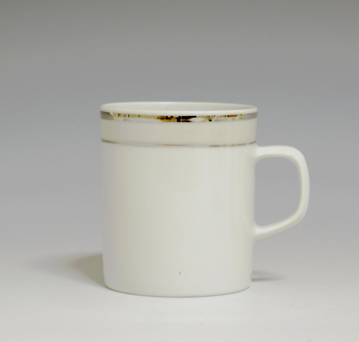 Kopp av porselen med hvit glasur. Dekorert med to enkle striper i platina med et grått bånd i mellom øverst på korpus.
Modell: Saturn
Dekor: Platina
