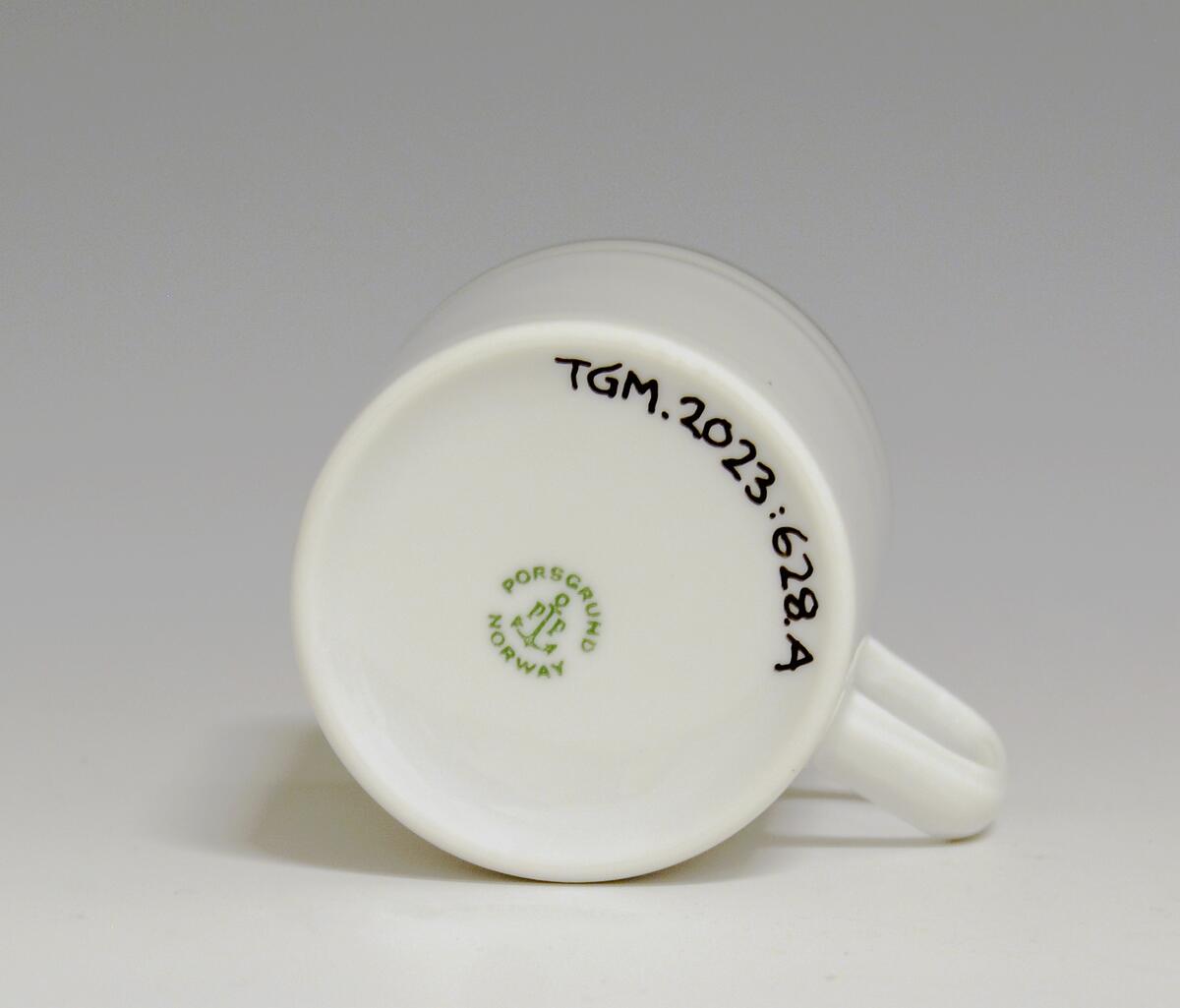 Kopp av porselen med hvit glasur. Dekorert med to enkle striper i platina med et grått bånd i mellom øverst på korpus.
Modell: Saturn
Dekor: Platina
