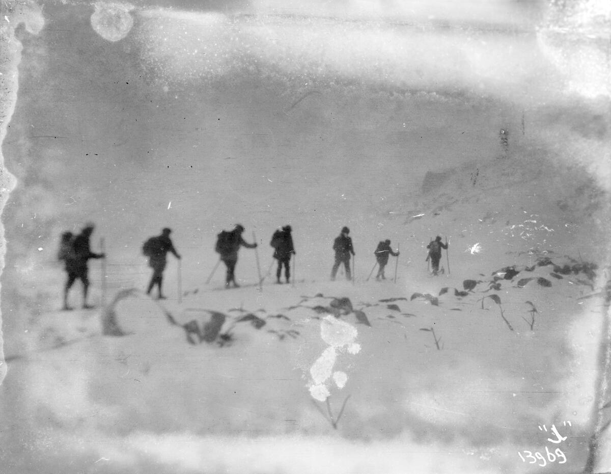 En gruppe på syv personer går på ski i et snødekket fjellandskap.