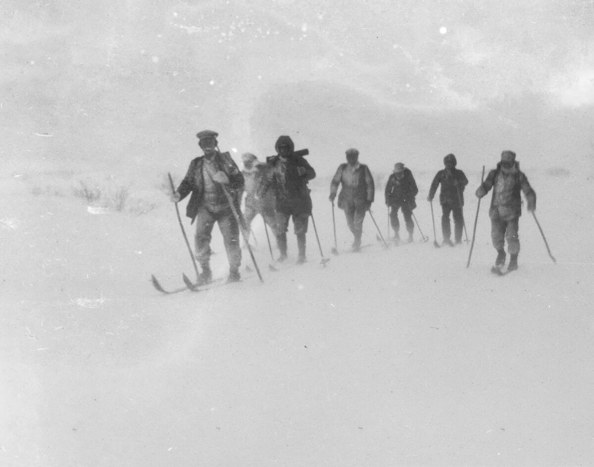 Sju menn på ski i et snødekket fjellandskap.