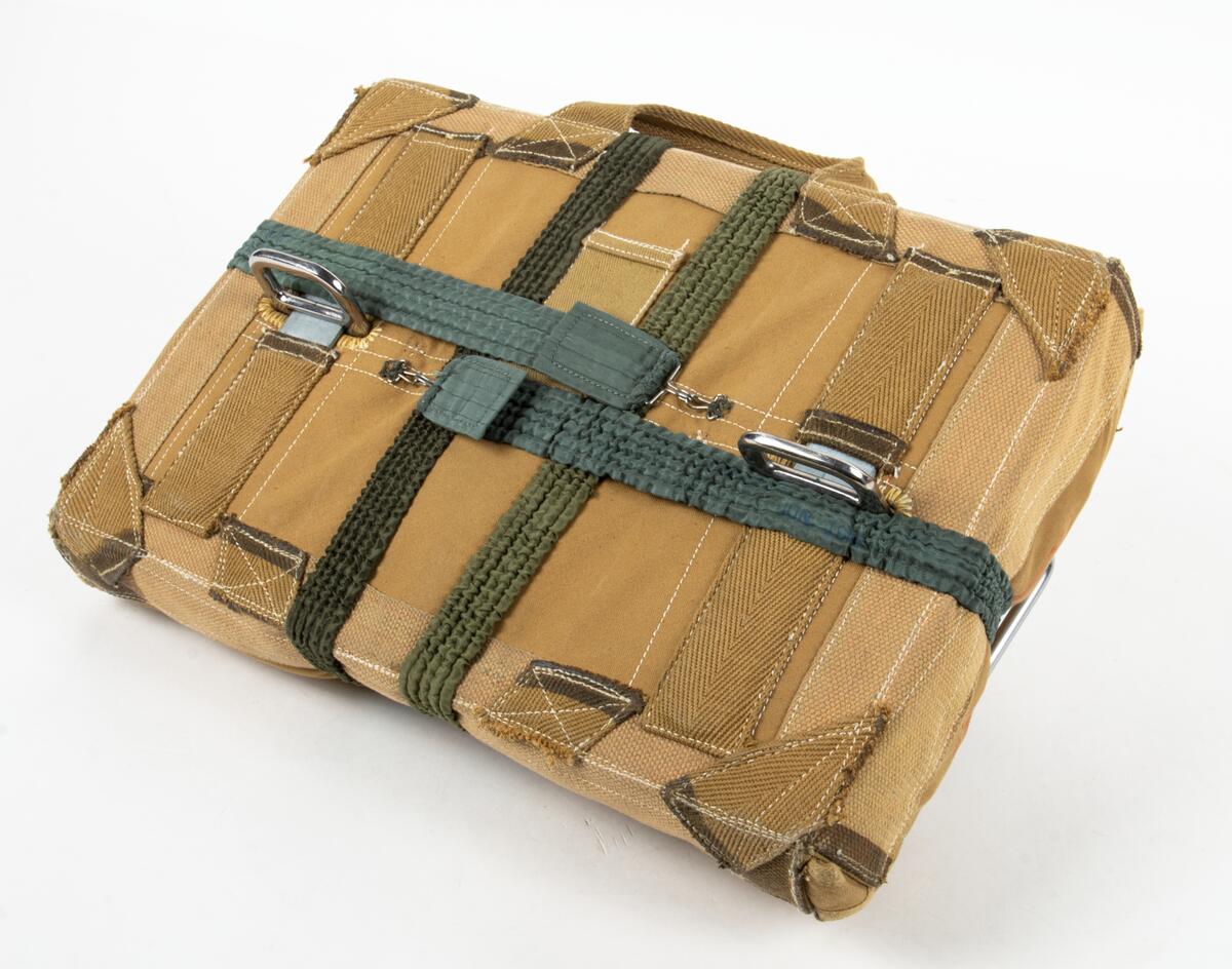 Bröstfallskärm, FASK 22. G.Q, Typ C. Mk.2.
Remmarnas utlösningsmekanism är helt mekanisk. Hölje av smärtingduk. Vit kalott av nylon. Skärmen är packad och stämplad Kasserad.
Medföljande sele med remmar av sadelgjord. Selen har individnumer 3834 och en etikett med texten; "Tillverkad av Irvin Fallskärmsaktiebolag Stockholm Sverige". (Osäkert om selen tillhör fallskärmen.)