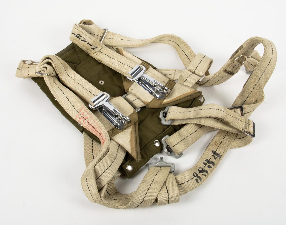 Bröstfallskärm, FASK 22. G.Q, Typ C. Mk.2.
Remmarnas utlösningsmekanism är helt mekanisk. Hölje av smärtingduk. Vit kalott av nylon. Skärmen är packad och stämplad Kasserad.
Medföljande sele med remmar av sadelgjord. Selen har individnumer 3834 och en etikett med texten; "Tillverkad av Irvin Fallskärmsaktiebolag Stockholm Sverige". (Osäkert om selen tillhör fallskärmen.)