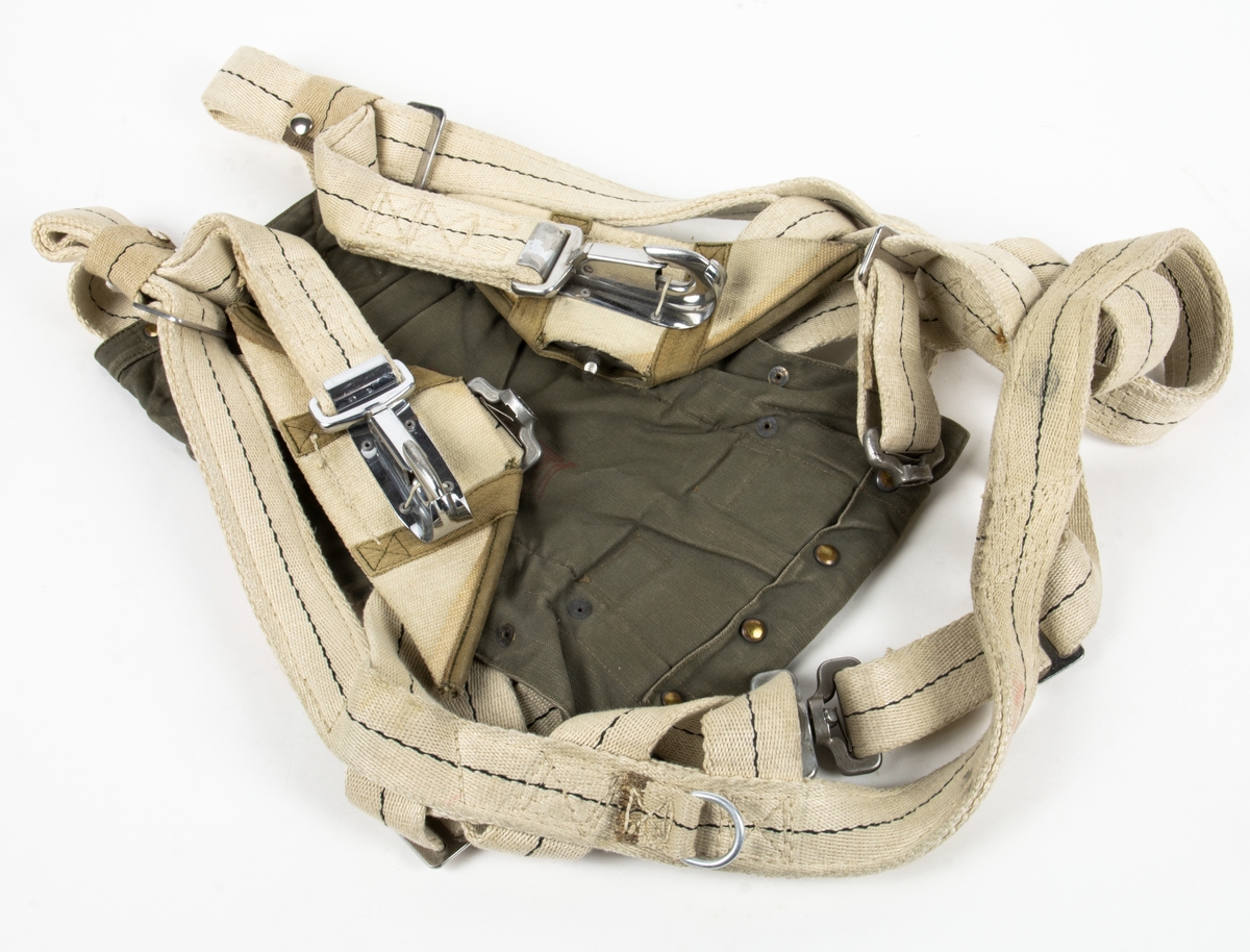 Bröstfallskärm, FASK 22. G.Q, Typ C. Mk.2.
Remmarnas utlösningsmekanism är helt mekanisk. Hölje av smärtingduk. Vit kalott av nylon. Skärmen är utlöst och stämplad Kasserad.
Medföljande tillhörande sele med remmar av sadelgjord.