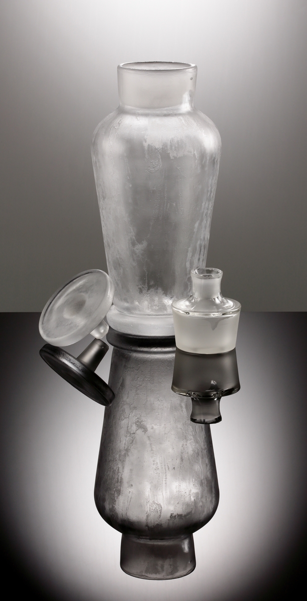 Formgiven av Vicke Lindstrand. Cocktailshaker med rund klackfot. Tillhörande issnipa och cylindrisk propp.
Isad yta.