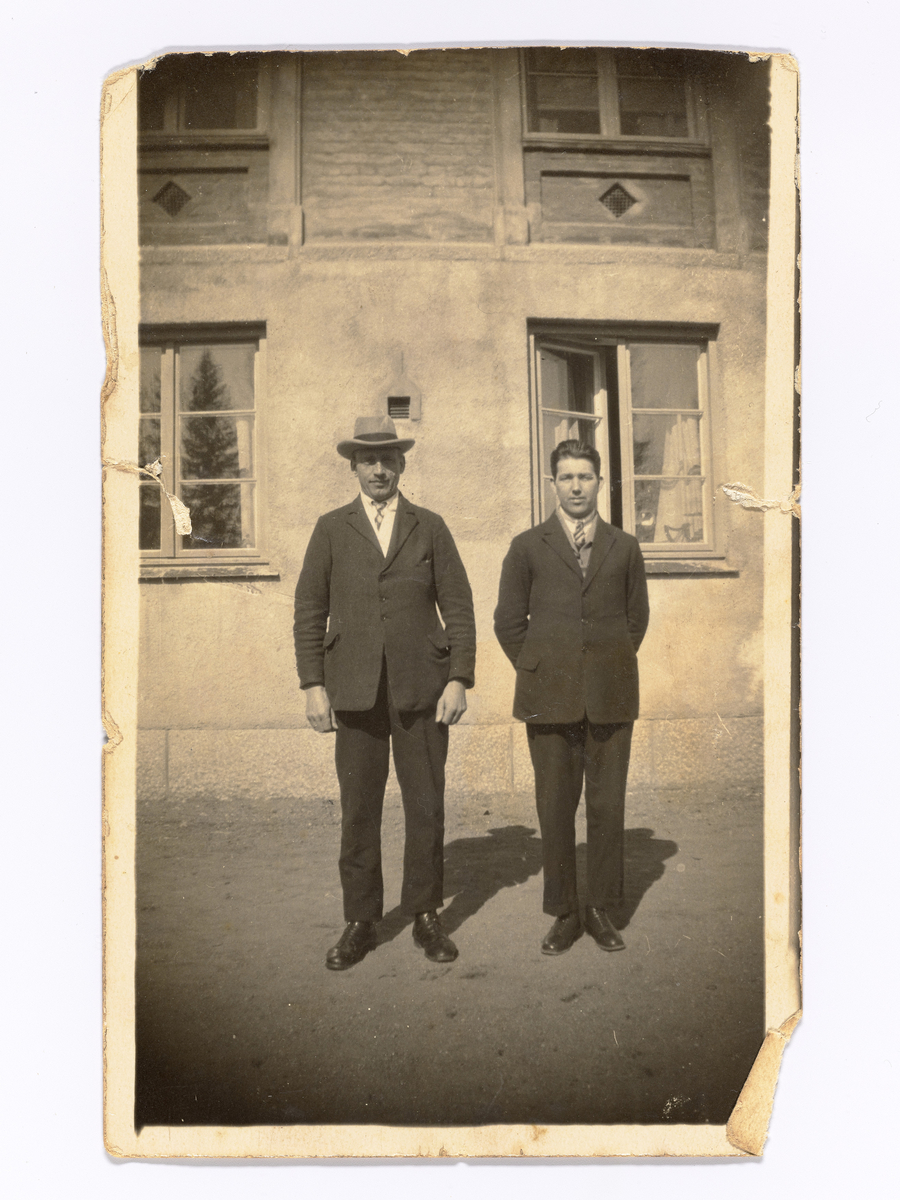 To menn i dress oppstilt fremfor en murbygning