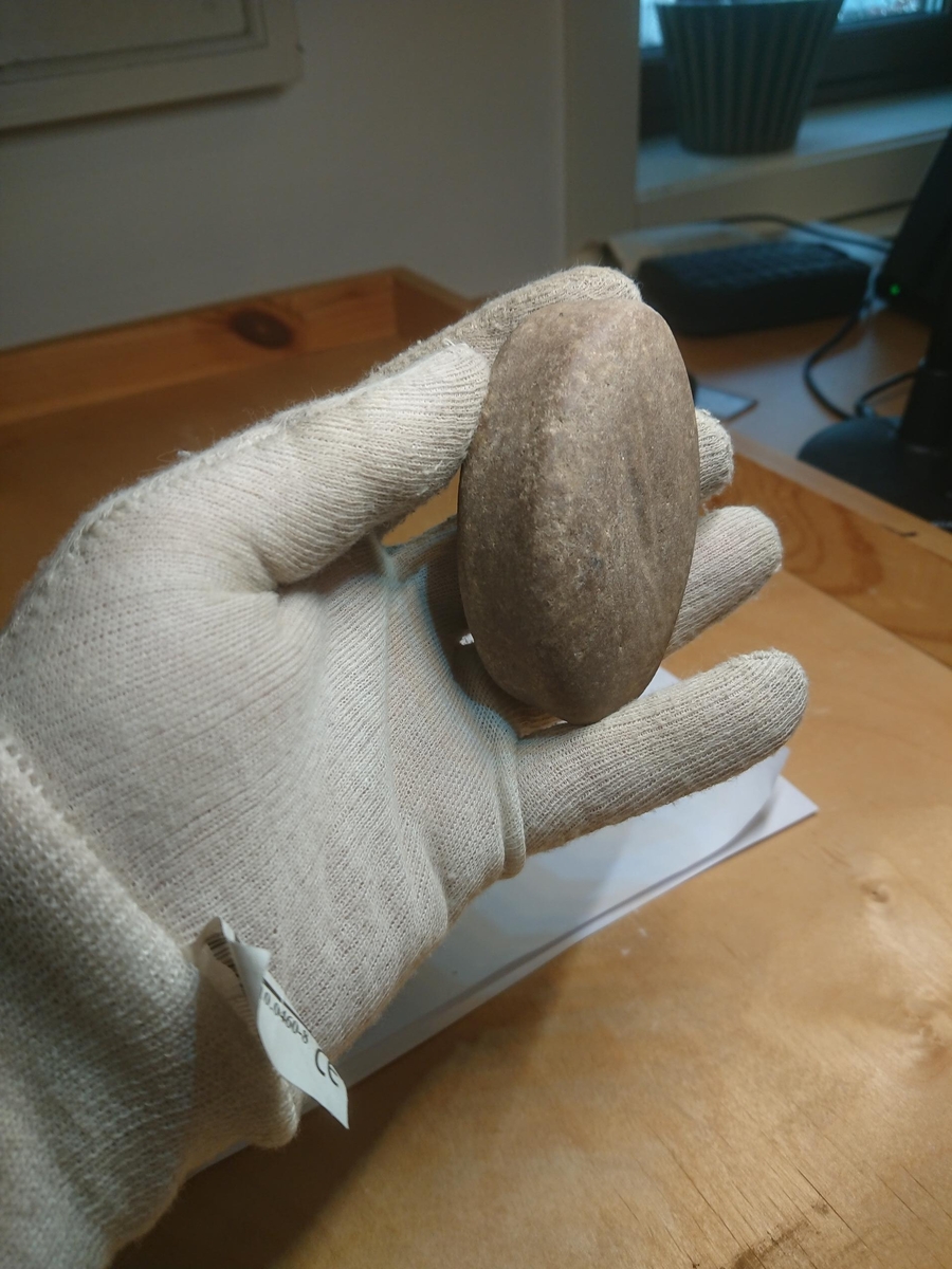 En komplett ildslagingsstein, type beltestein. Typologisk datert til romertid - folkevandringstid. Fargen er grå til gråbrun. Med distinkte bruksspor/furer på begge breisidene. Oval form, med kortsidene utformet svakt konkavt hele veien rundt, for å passe inn med et belte. Ikke med smalt hakk for snor. Kortsidene er glattslipte. Form ligner på for eksempel T 682, C 1743. Største bredde på midten av breisidene er ca. 7,5 cm, smalner inn mot endene til ca. 2,5 cm. Samme tykkelse på hele gjenstanden, ca. 2,5 cm. Total lengde er ca. 7,5 cm. Objektet har ingen skader.
"I Skandinavia brukte man i eldre jernalder et stykke av bergarten kvartsitt, kalt ildslagningsstein eller beltestein fordi den ble båret i beltet, og en jernbit. Når man slo jernet langs en rille i steinen, kunne gnistene få tørr knusk til å fatte ild." (SNL)
Fnr. 201157