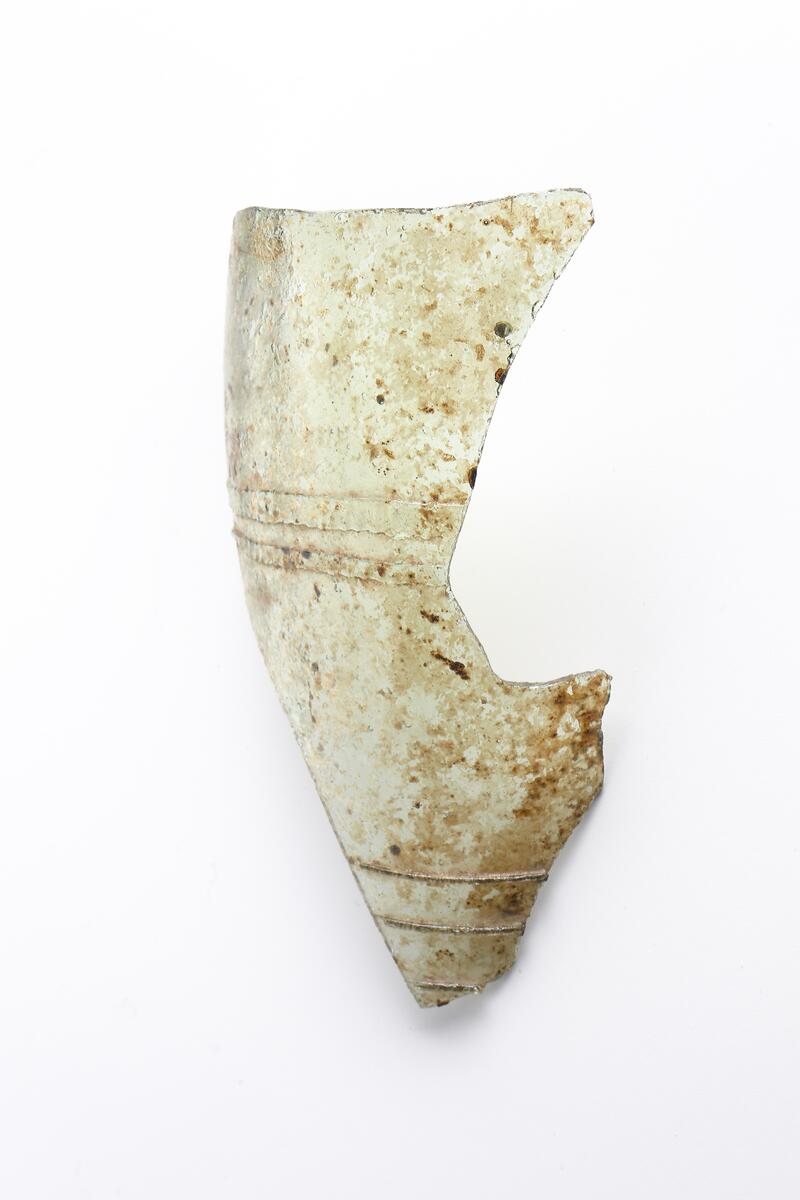 Del av buken på ett ofärgat, kägelformat, optikblåst passglas som är ornerat med fem pålagda parallella trådar. De två övre trådarna är strierade. Fragmetet har glaspest.