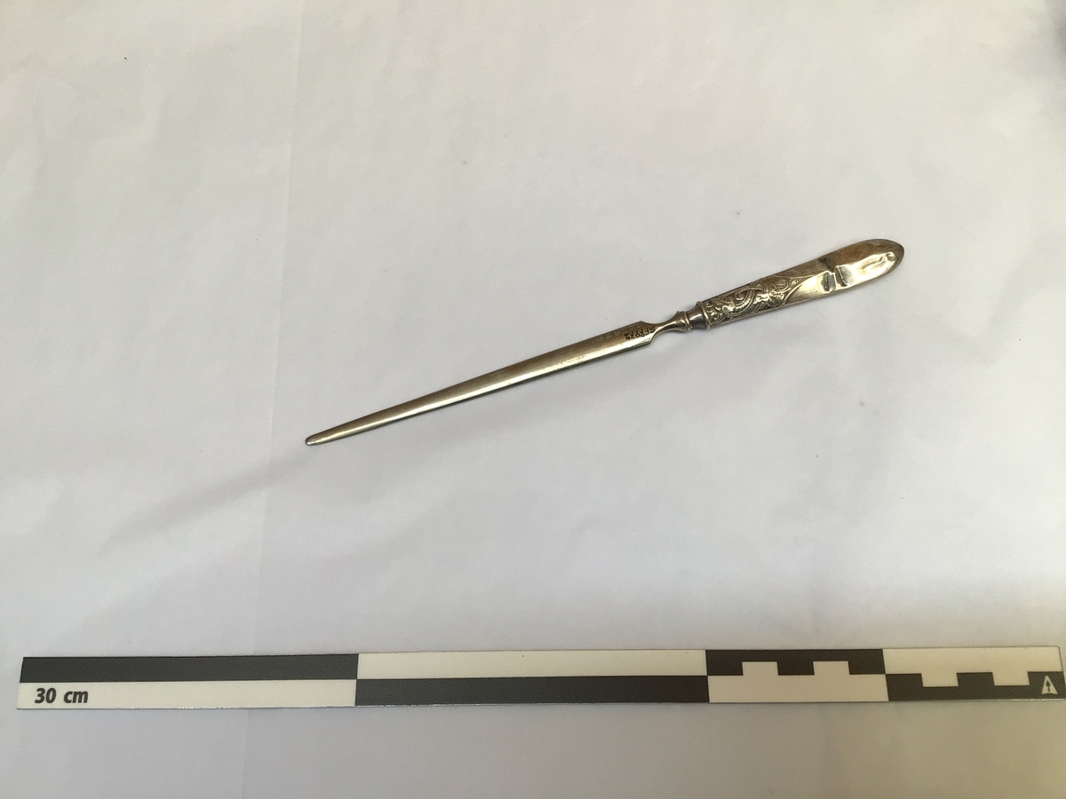 Knivforma med tveegga knivblad, skarpt nok til å opna kovolutter. Handtaket eller skaftet har dragemotiv.