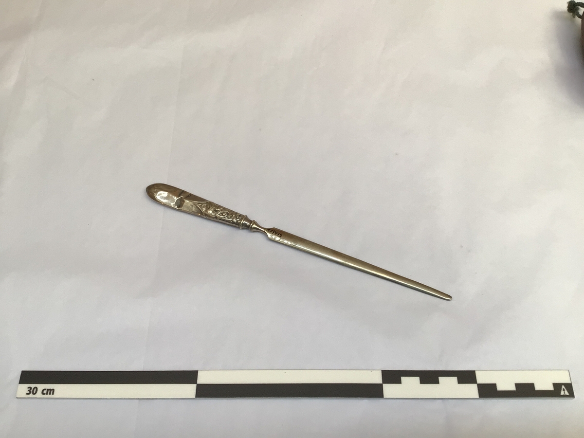 Knivforma med tveegga knivblad, skarpt nok til å opna kovolutter. Handtaket eller skaftet har dragemotiv.