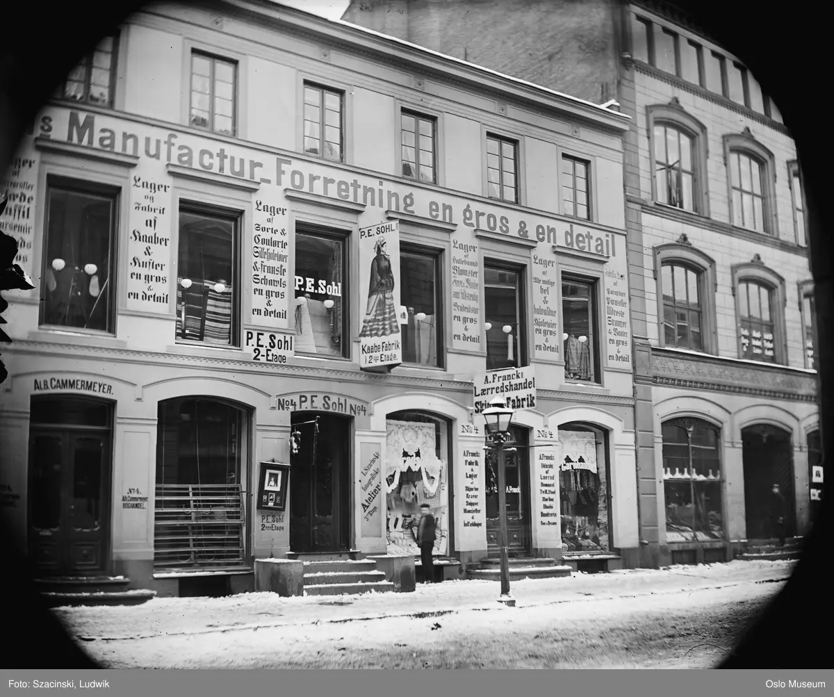 forretningsgård, P.E. Sohls manufakturforretning, A. Francks Lærredshandel og skilt fotograf L. Szacinskis utstillingskasse og skilt, gatebelysning, gutt, snø