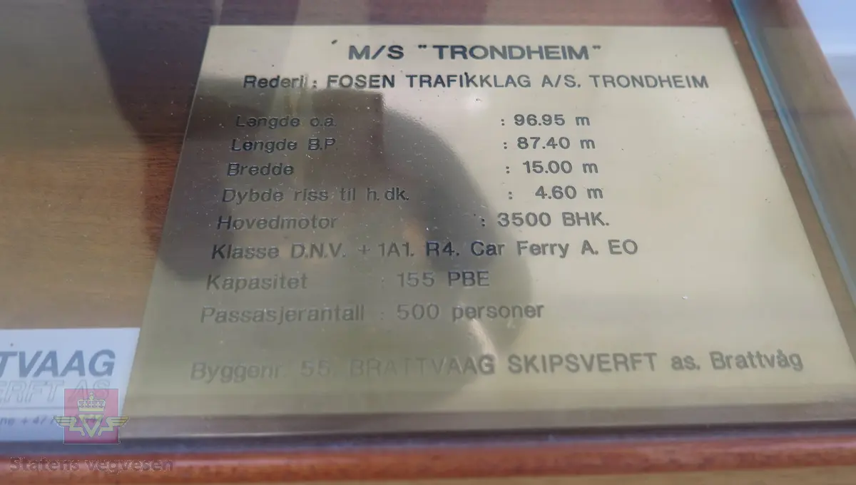 Ferjemodell i monter. I hovedsak svart og hvit modell i brun monter, Monteren er av tre og glass. Monteren har en plakett med fakta om ferja, samt merking fra rederiet og modellbygger.