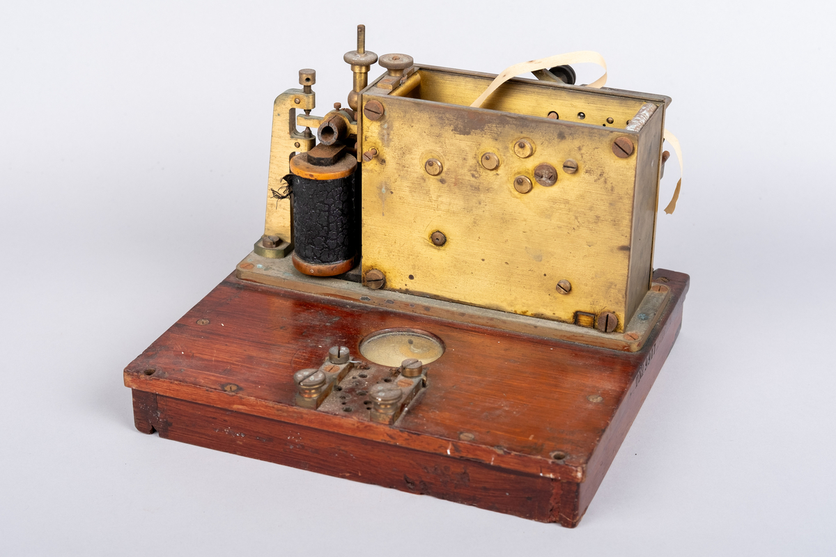 Et morseapparat av typen Siemens & Halske (Berlin) No. 19256. Apparatet har en base av rødmalt treverk og apparatet festet på toppen. Basen har en skuff hvori en papir rull er instarert og innført i apparatet. Basen har på den ene siden et vindu hvor papir rullen kan sees.