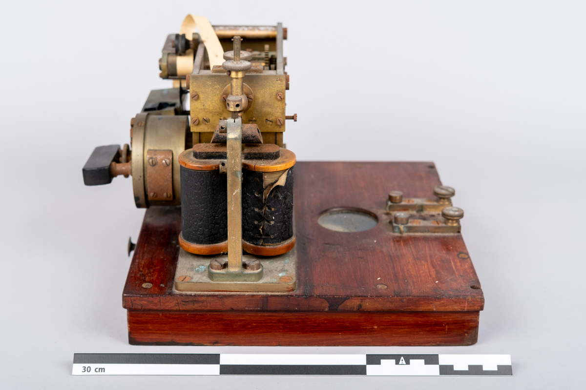 Et morseapparat av typen Siemens & Halske (Berlin) No. 19256. Apparatet har en base av rødmalt treverk og apparatet festet på toppen. Basen har en skuff hvori en papir rull er instarert og innført i apparatet. Basen har på den ene siden et vindu hvor papir rullen kan sees.