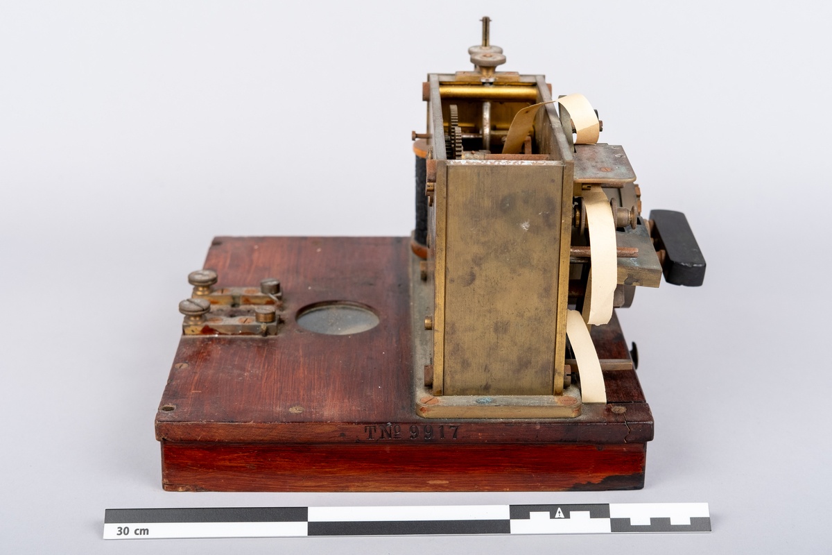 Et morseapparat av typen Siemens & Halske (Berlin) No. 19256. Apparatet har en base av rødmalt treverk og apparatet festet på toppen. Basen har en skuff hvori en papir rull er instarert og innført i apparatet. Basen har på den ene siden et vindu hvor papir rullen kan sees.