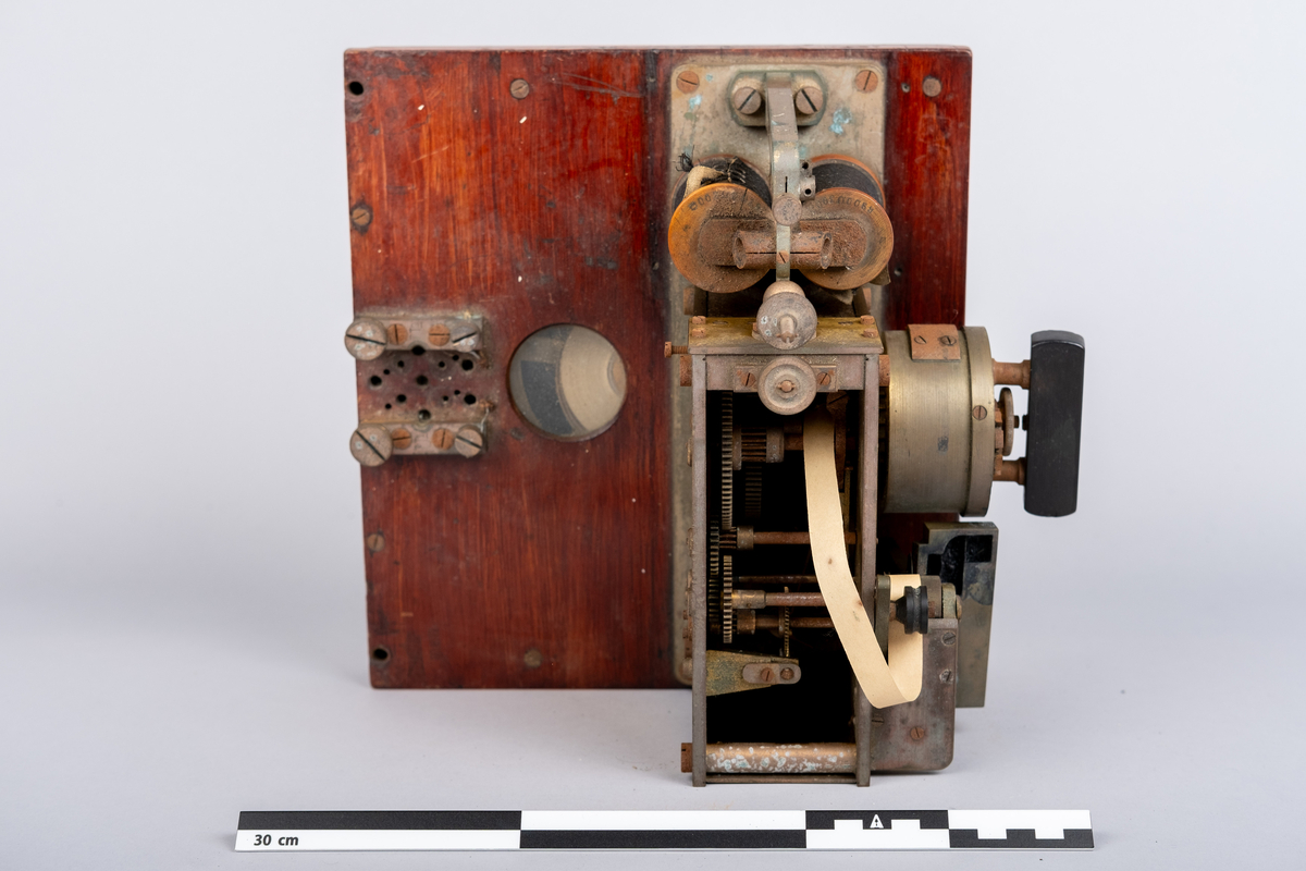Et morseapparat av typen Siemens & Halske (Berlin) No. 19256. Apparatet har en base av rødmalt treverk og apparatet festet på toppen. Basen har en skuff hvori en papir rull er instarert og innført i apparatet. Basen har på den ene siden et vindu hvor papir rullen kan sees.