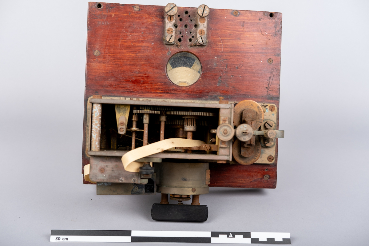 Et morseapparat av typen Siemens & Halske (Berlin) No. 19256. Apparatet har en base av rødmalt treverk og apparatet festet på toppen. Basen har en skuff hvori en papir rull er instarert og innført i apparatet. Basen har på den ene siden et vindu hvor papir rullen kan sees.