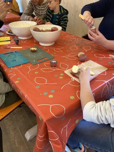 Barn og voksne sitter rundt et bord og lager potettrykk.