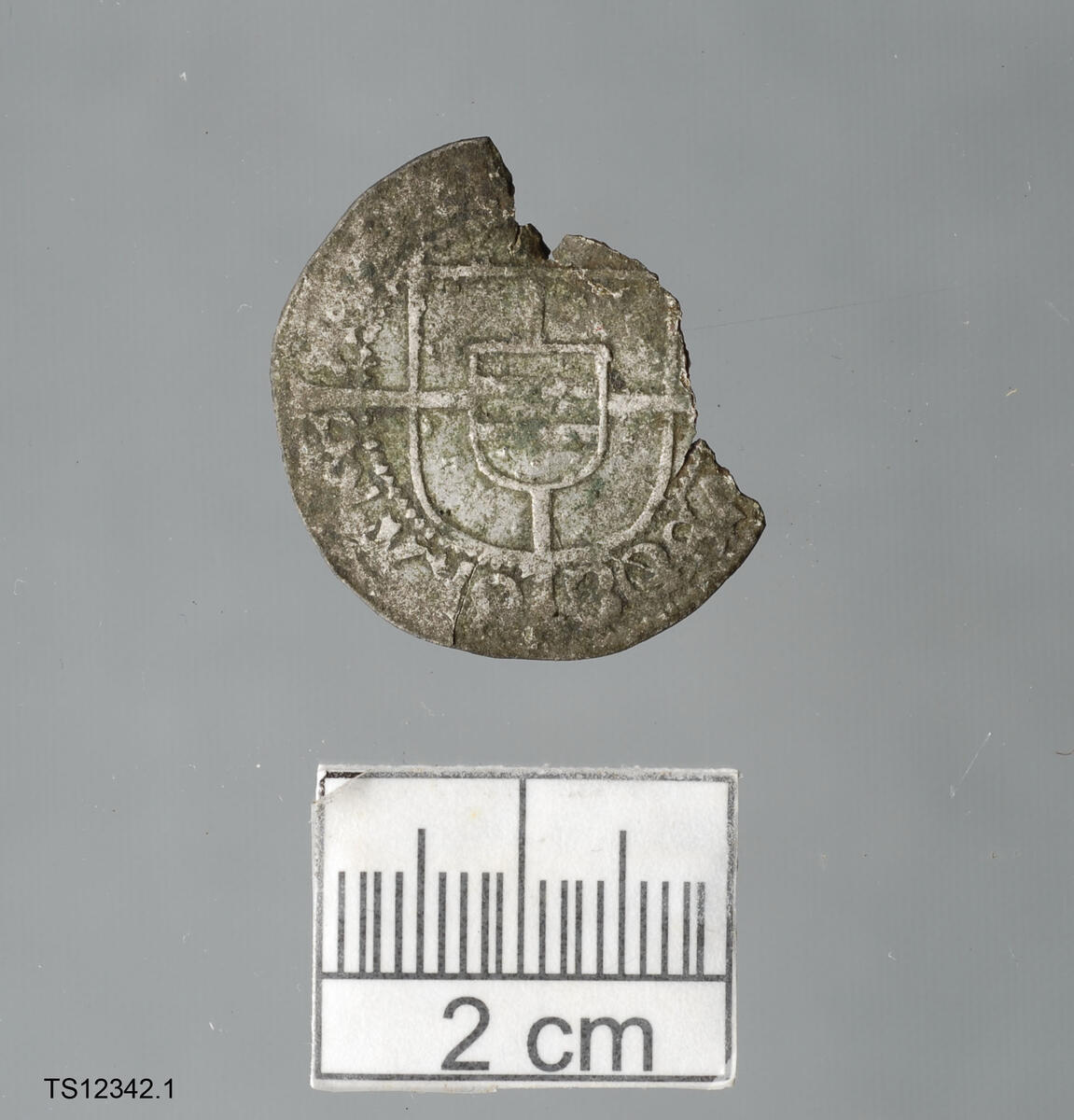 Mynt av sølv, 1 stk, av type skilling fra 1525, slått i Oslo. 2,6 cm i diameter.1,2 gram. 
