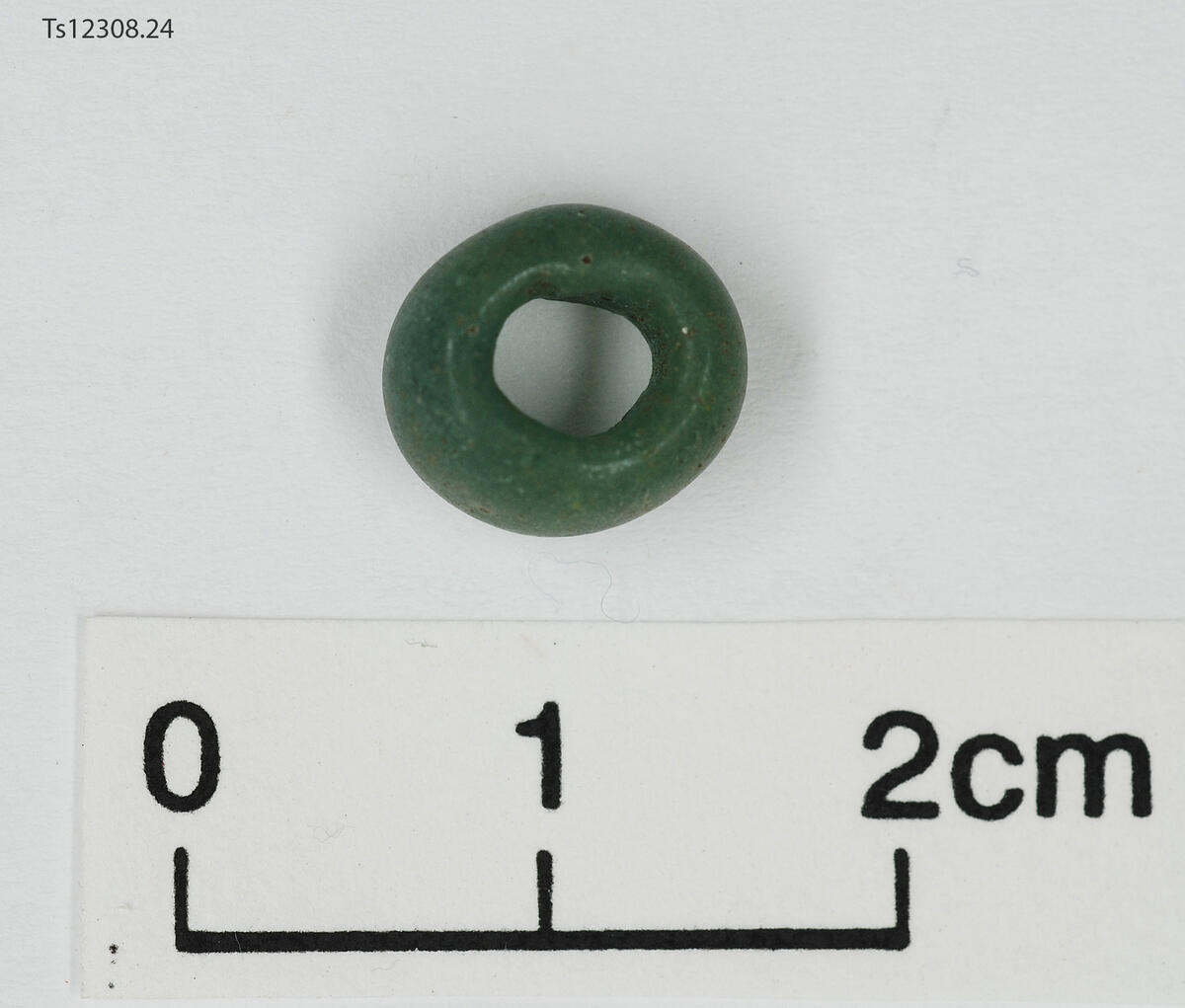 1 stk perle av glass. Grønn. Rund, ujevn form stort trådhull. 1 cm i diameter, 0,6 cm tykk.