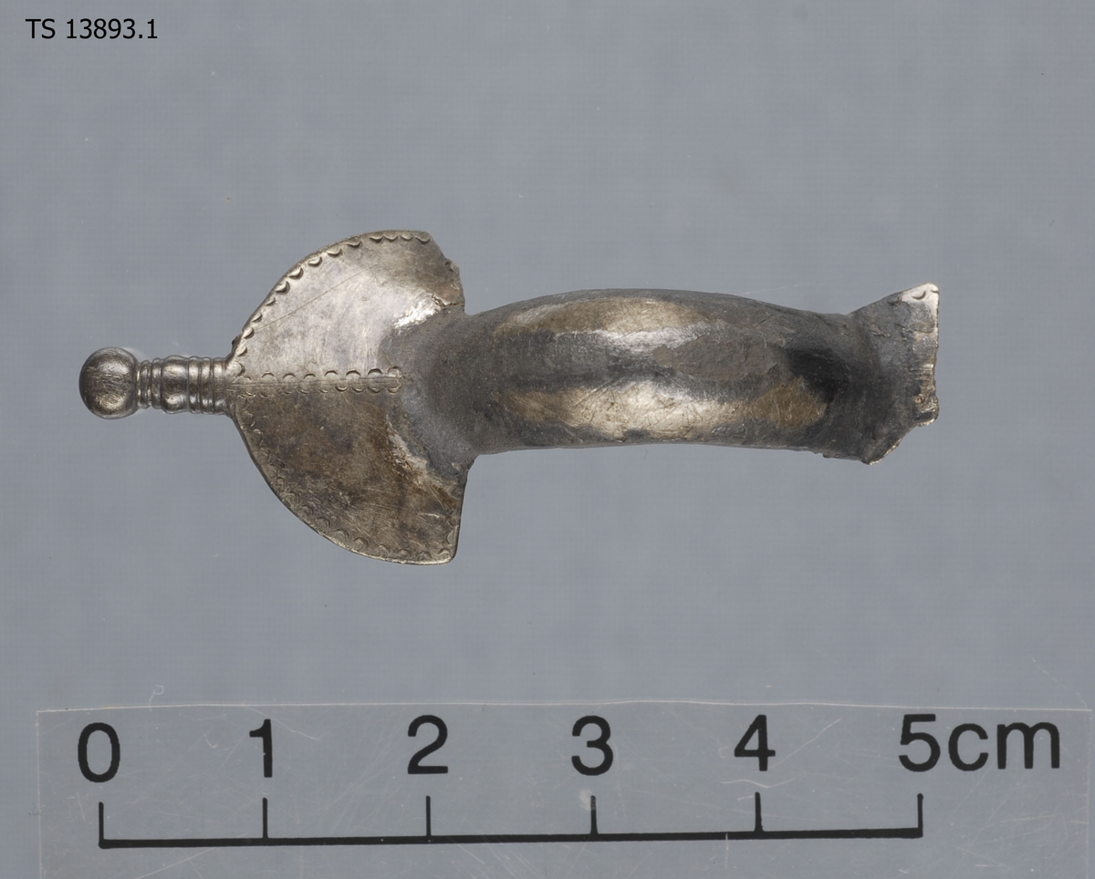 Liten fibula av bronse belagt med sølv. Stl: 5,16 cm, Stb:2,11 cm. Toppplaten og bakspennen er brukket av. Halsen er jevnt buet, det er heller ingen ornamentikk eller korsform på denne. Foten er spadeformet, og stiplet ned midten og langs bunnen. Nederst er en knopp, med fem fortykkede linjer rundt hele. Foten minner om Shetelig (1911:36) Fig. 38, mens formen på halsen minner om Shettelig (1911:35) Fig. 37. Ligner i form og Müller (1897:523) Fig.324. Dateres på bakgrunn av Shetelig (1911) og Müller (1897) til Folkevandringtid. Mål: T: 0,17 cm, Stl: 5,16 cm, Stb: 2,11 cm. Vekt: 10,12 g. 