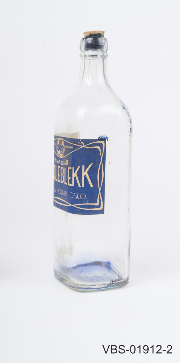 Glassflaske for skoleblekk. Firkantet gejnnomsiktig flaske med kork. 
Stor etikett på 3 sider, tekst på norsk.