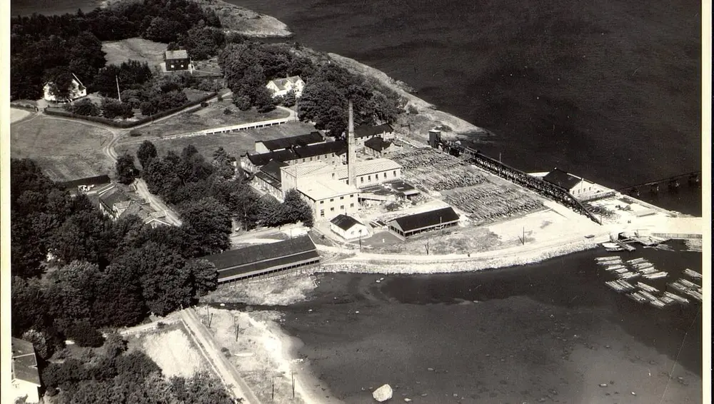 Sort-hvitt-bildet viser et fabrikkområde som ligger rett ved sjøen